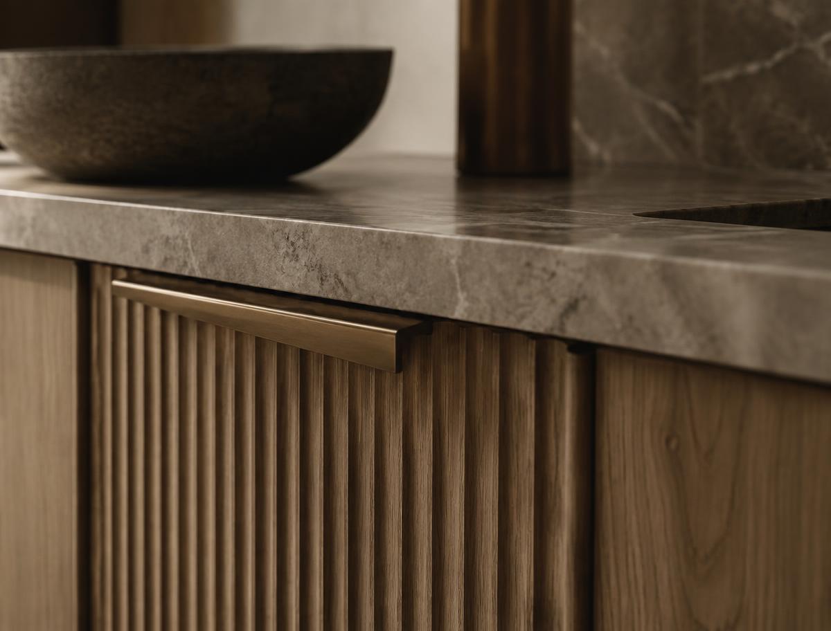 Fluted oak cabinetry with a brushed bronze handle and stone worktop